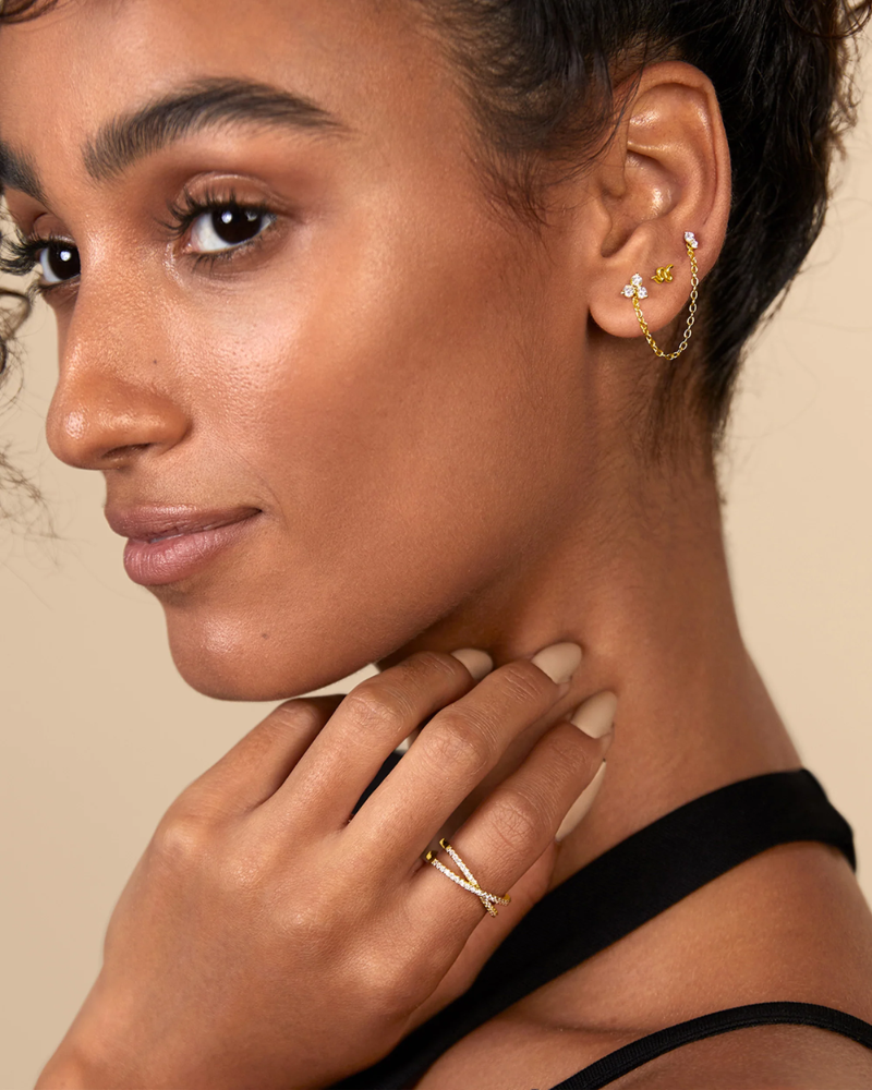 Close-up of a woman wearing gold earrings and rings on a beige background