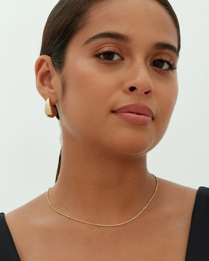 Woman wearing a gold necklace and hoop earrings on a plain background